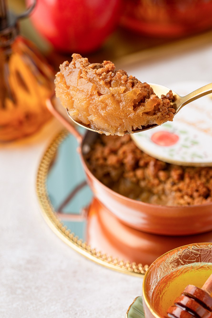 Colherada de crumble de maçã saindo da panelinha de cobre